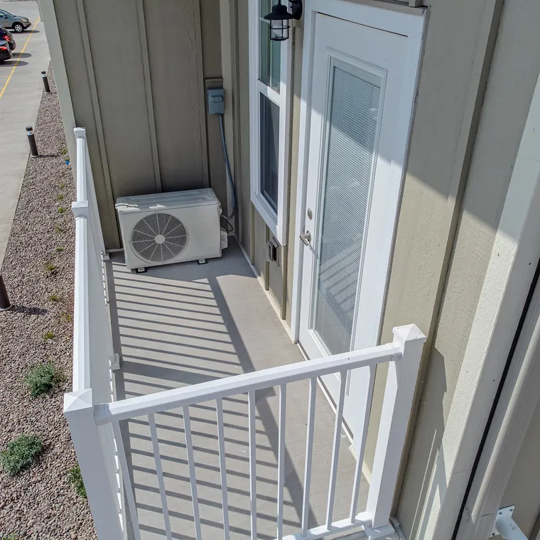 A heat pump outdoor unit installed on an apartment balcony in a tight space beside a railing.