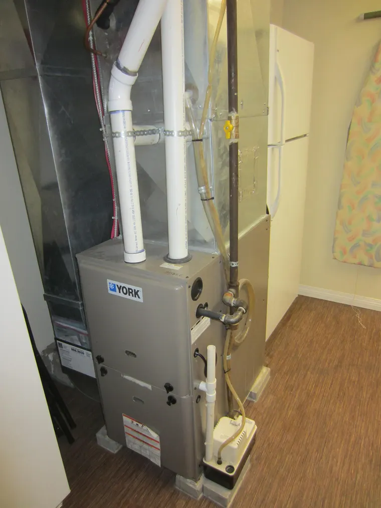 A condensing forced air natural gas furnace installed in a basement, with its flue and supply ducting connected.