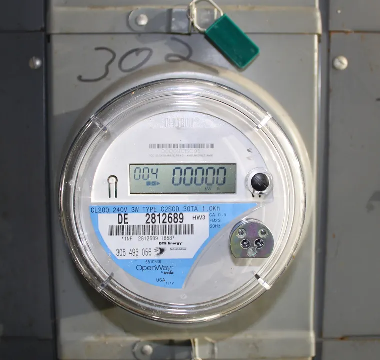 A residential smart electricity meter mounted on an exterior wall, its digital display showing a reading.