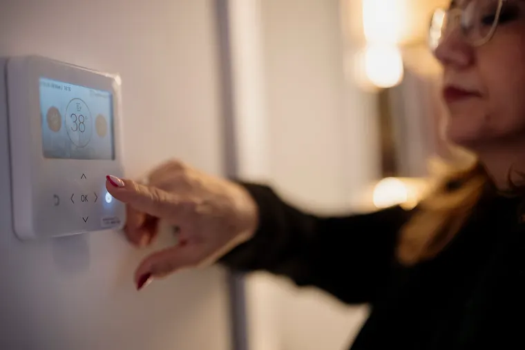 A hand adjusting the temperature on a wall mounted digital thermostat inside a home.